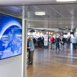 Digital signage display in a busy NYC terminal advertises flights, showcasing dynamic content management.