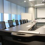 Image is of a conference room in a modern office with a projector screen on the wall.