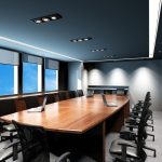 Image is of a corporate conference room with a brown table, black chairs, and bluish grey paint on the walls.